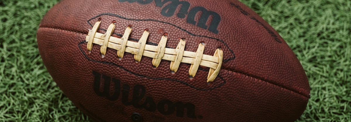 A football resting on turf, photographed close enough to show the laces.