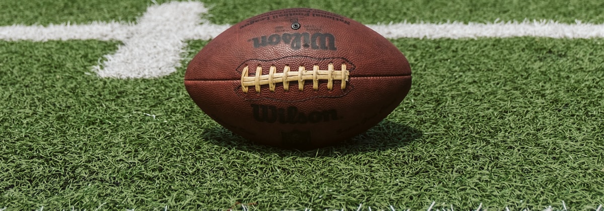 A football on a marked field, side on, with a yard line behind it.