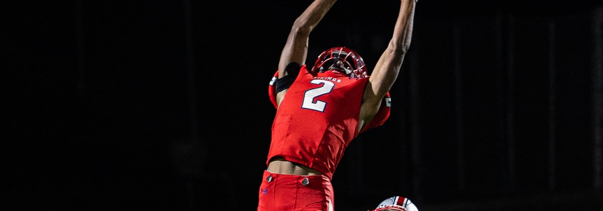 A receiver rising with both arms above his head to take a catch under floodlights.